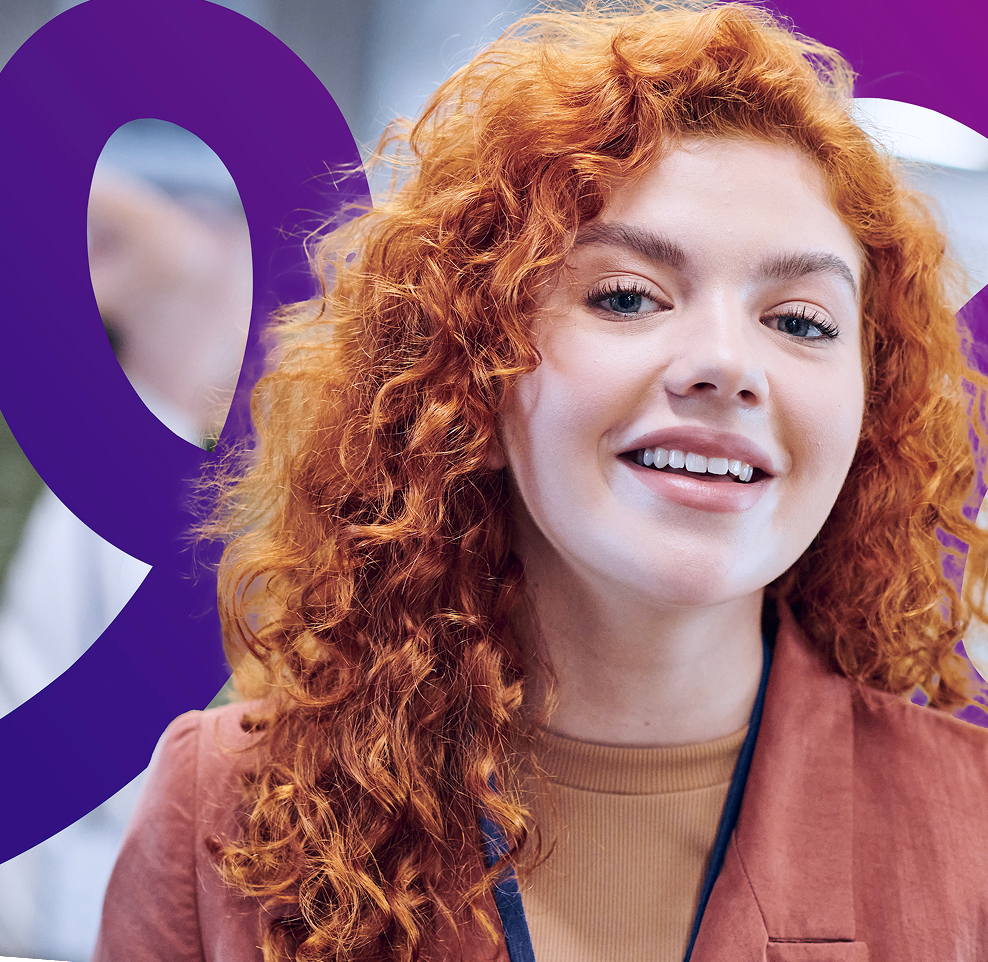 A young woman with curly red hair and fair skin smiles at the camera, wearing a pink blazer over a beige top. A bold purple abstract design is in the background.