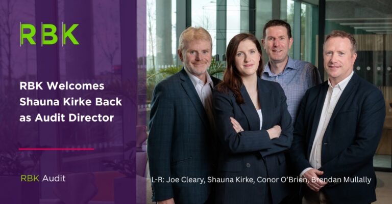 Four professionally dressed people, three men and one woman, stand together smiling in an office. Text on the left says, “RBK Welcomes Shauna Kirke Back as Audit Director.” Names are listed at the bottom of the image.